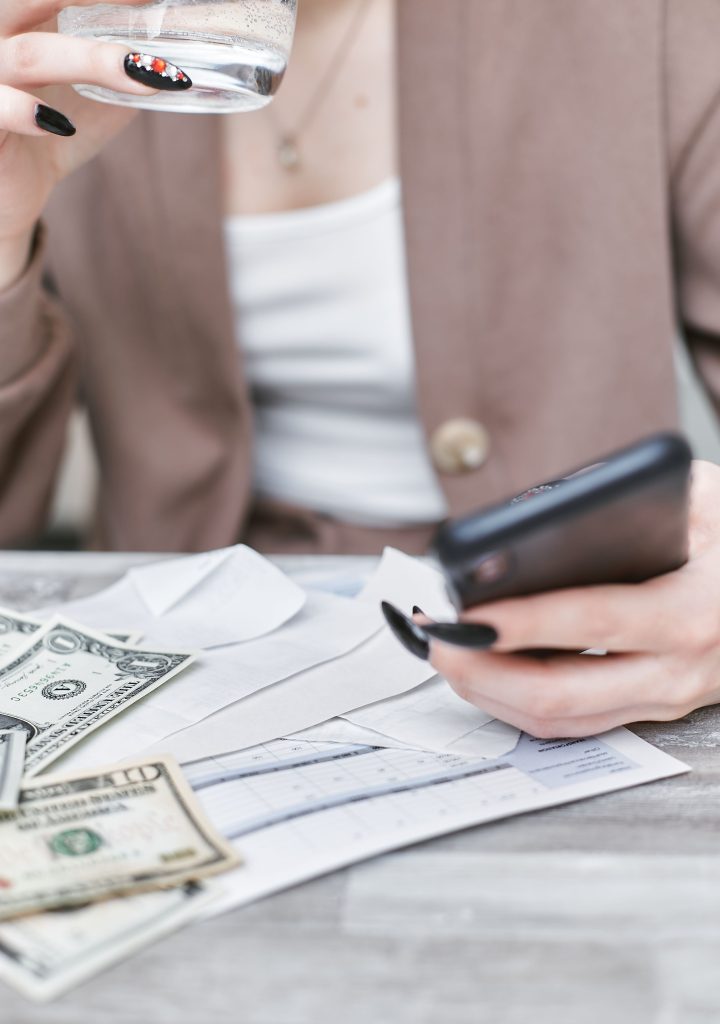 Person checking a phone at a desk covered with cash and bills