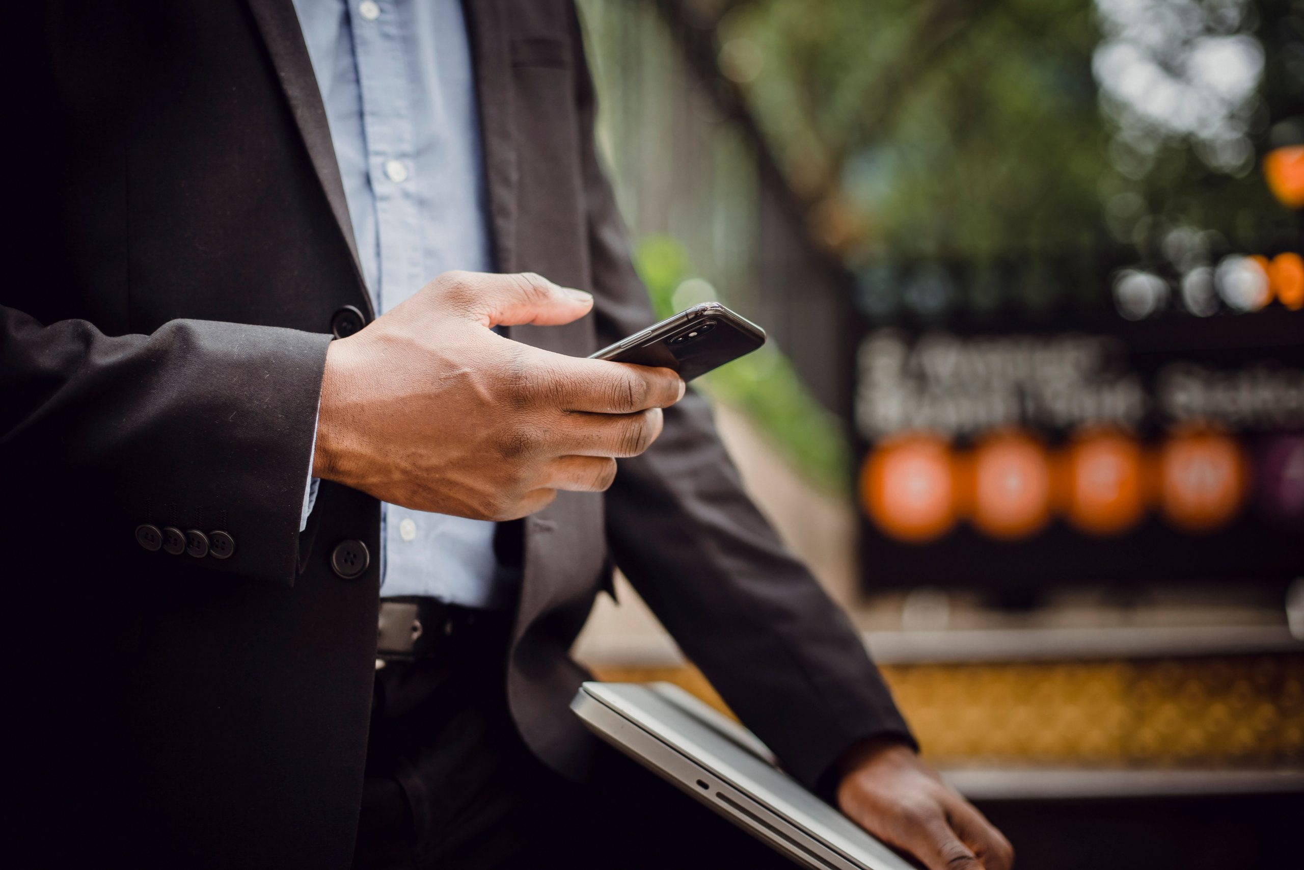Person in a suit holding a smartphone and a laptop on a city street
