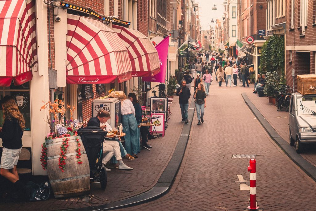 Narrow shopping street lined with small storefronts and awnings, people walking past