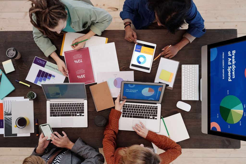 Overhead view of a team working around a table covered in laptops, tablets and charts