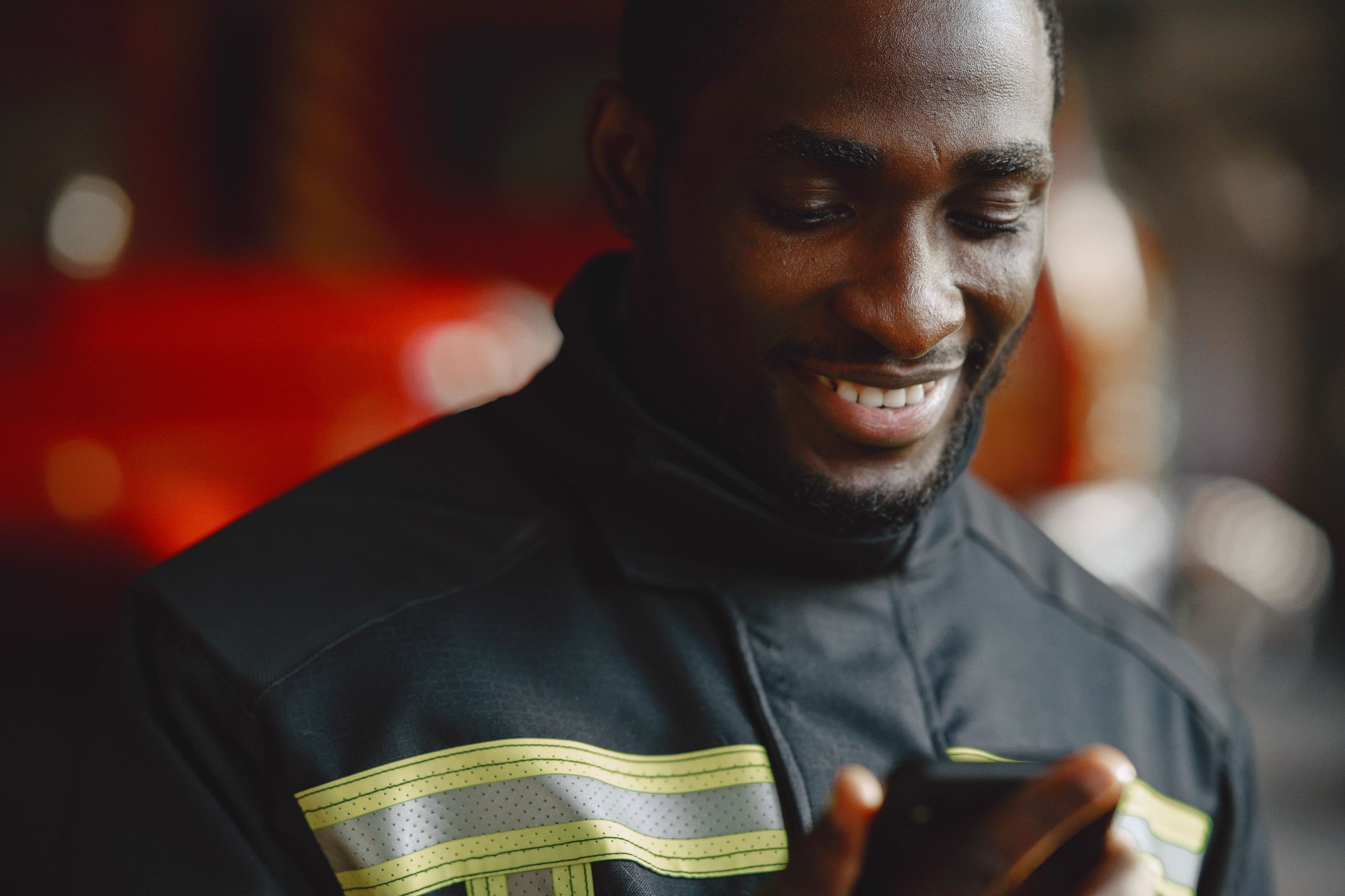 Smiling man in a work jacket with reflective stripes reading a text message on his phone